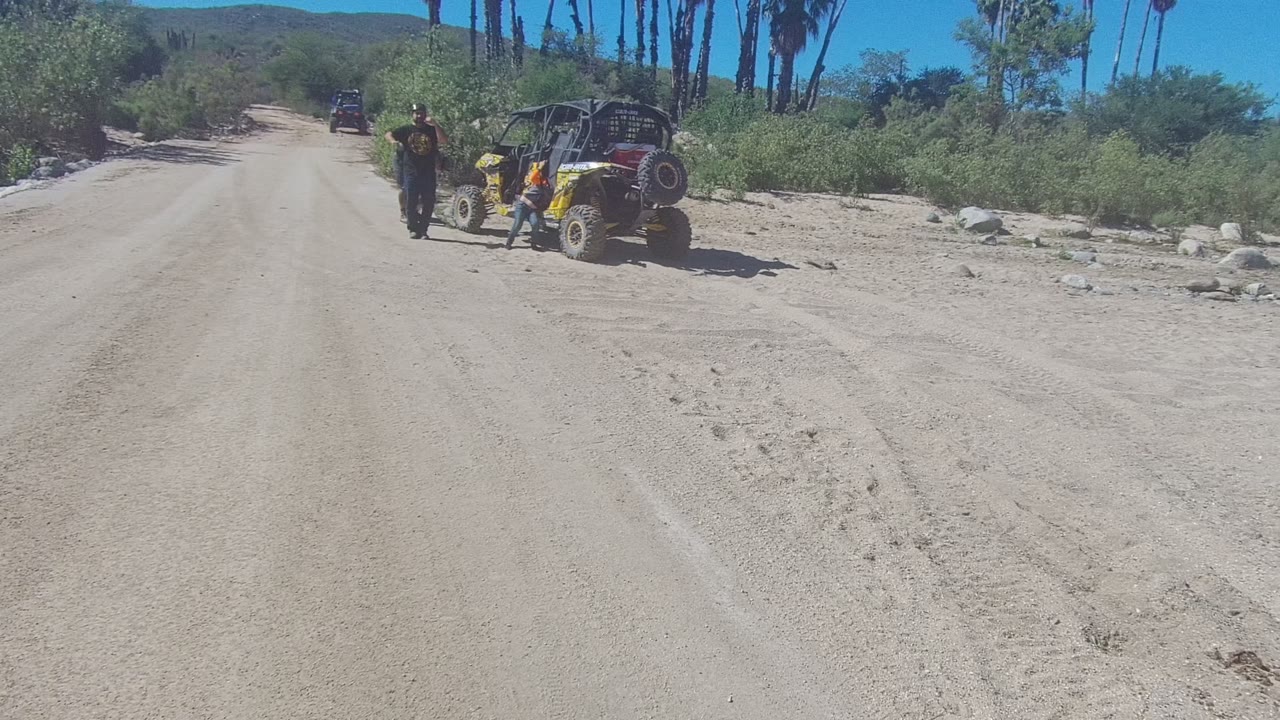 Yellow UTV beside a sandy road with one person walking nearby.