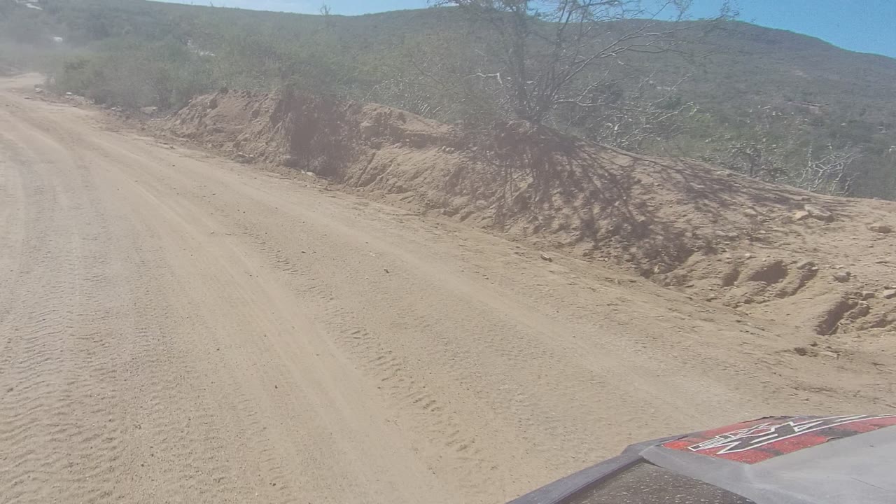 Forward view down a sandy dirt road bordered by dry vegetation.