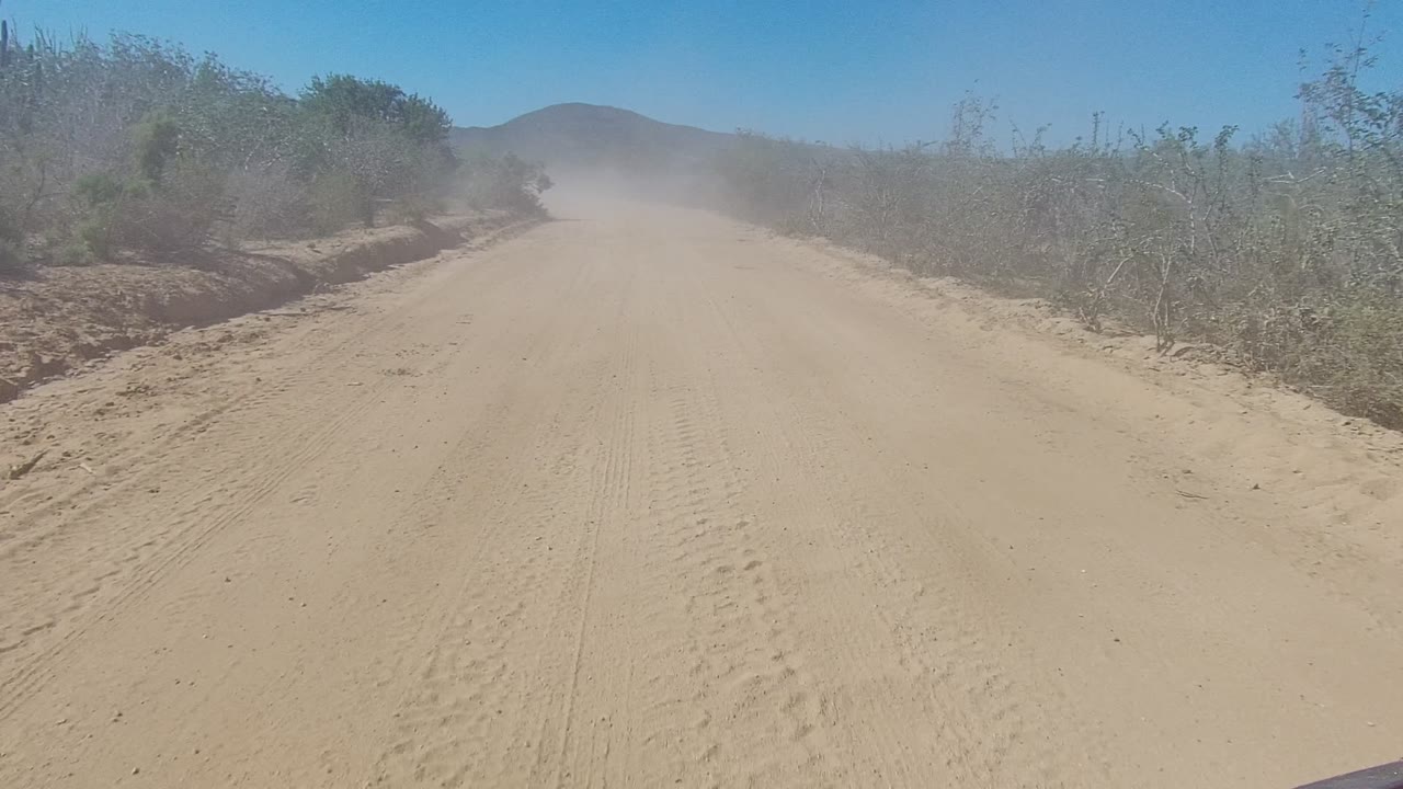 Sandy road curving through brush with dust ahead