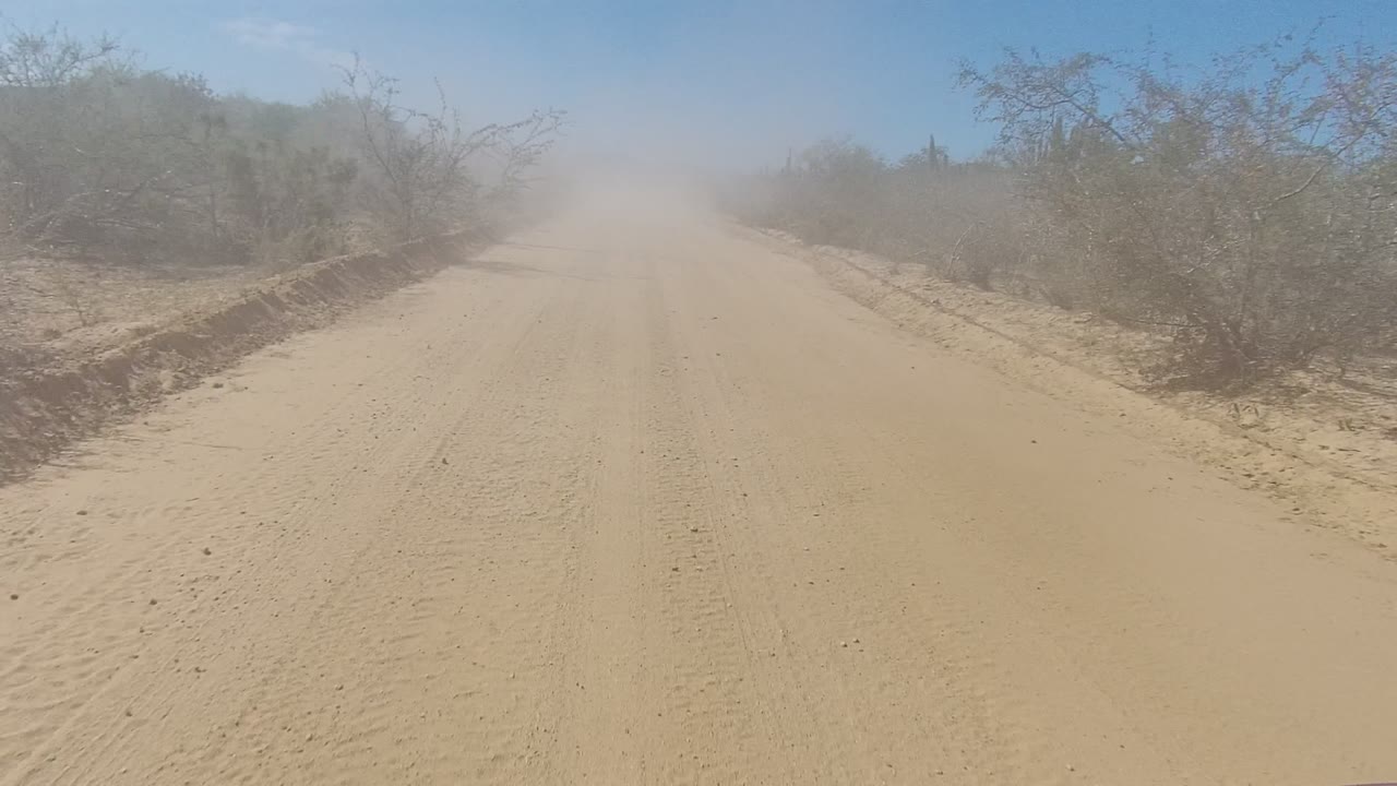 Straight dirt road with dust haze and sparse desert vegetation