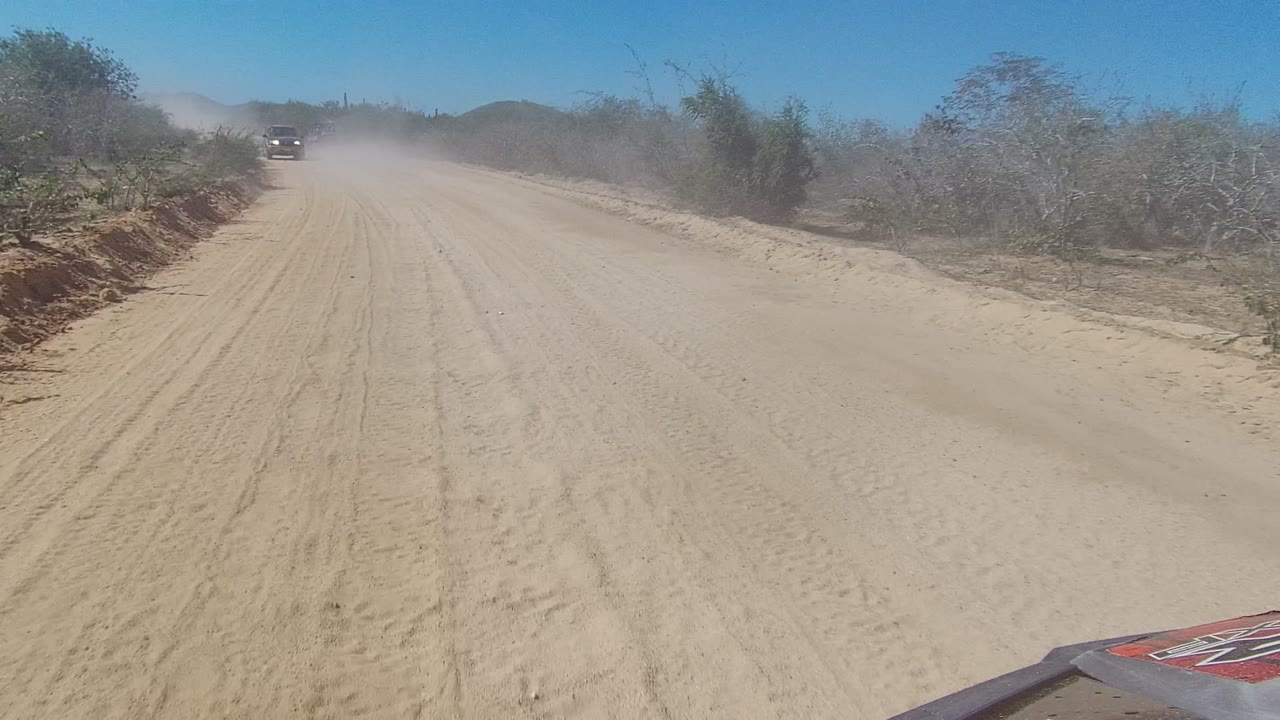 Vehicle ahead on a dusty dirt road through dry brush.