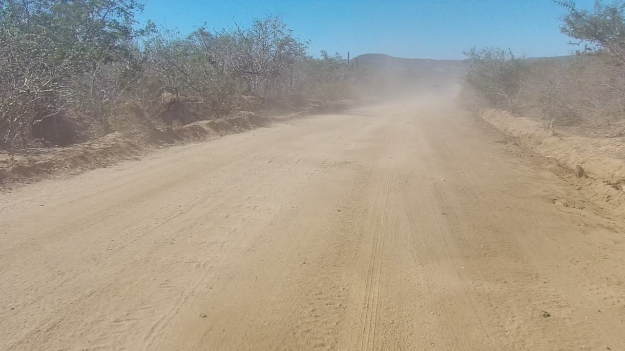 Straight dirt road with dust drifting in the distance.
