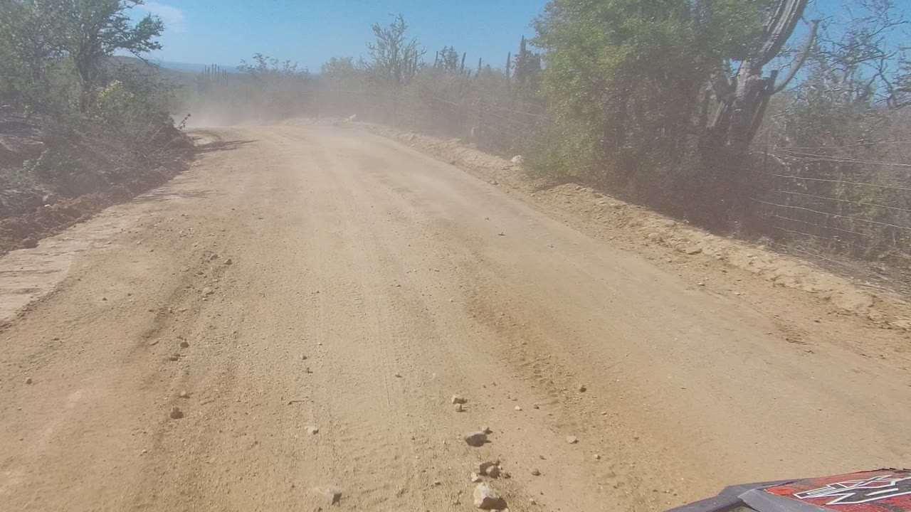 Vehicle view along a sandy road with dust ahead
