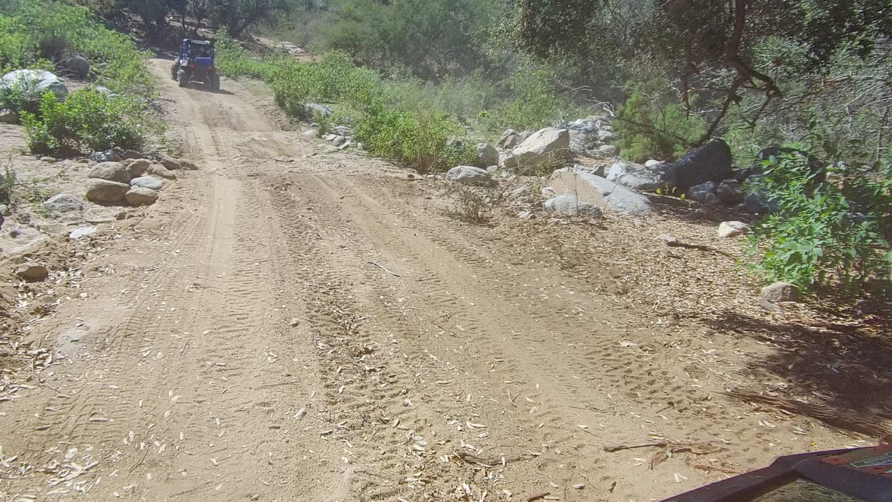 Dusty road curves through rocky brush with a small off-road vehicle ahead.