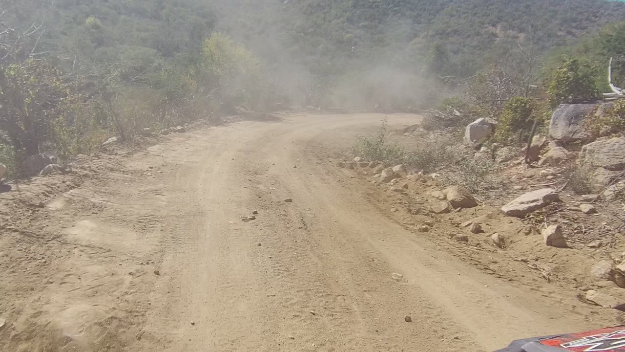 Straight dusty dirt road with rocks and scrub on both sides