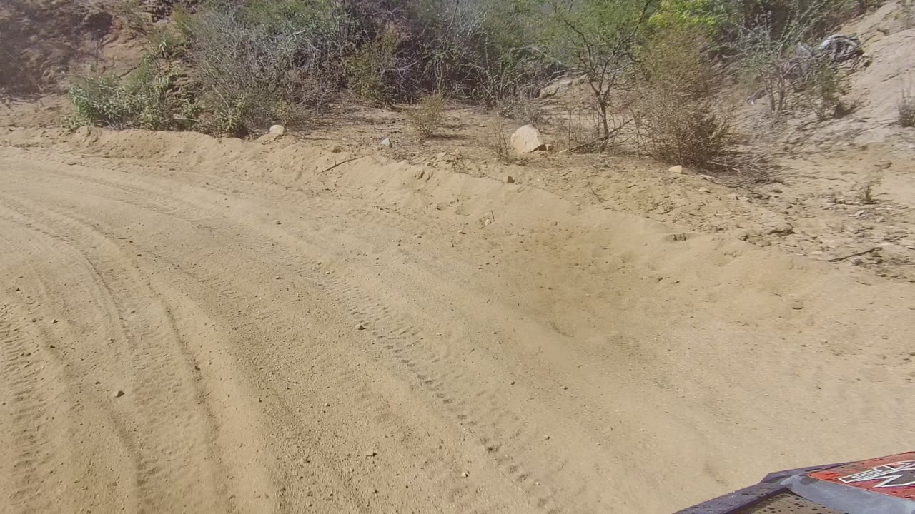 Dusty unpaved road with vehicle hood at lower right