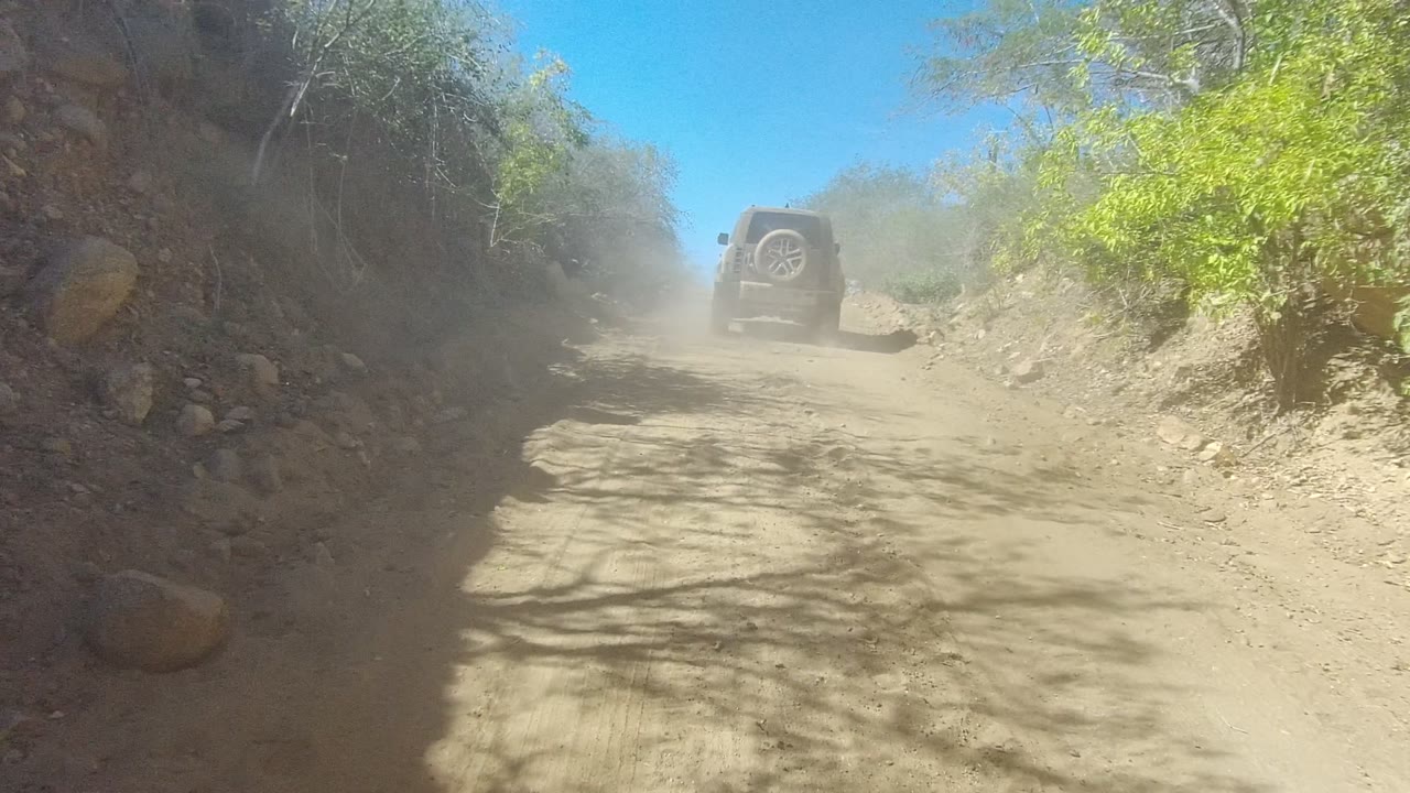 SUV farther up a dusty desert road with brush on both sides