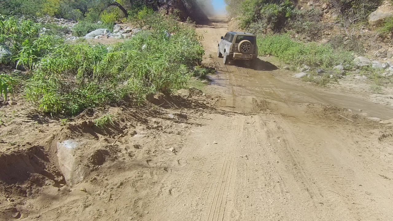 Off-road vehicle farther up a wet dirt path between rocky brush