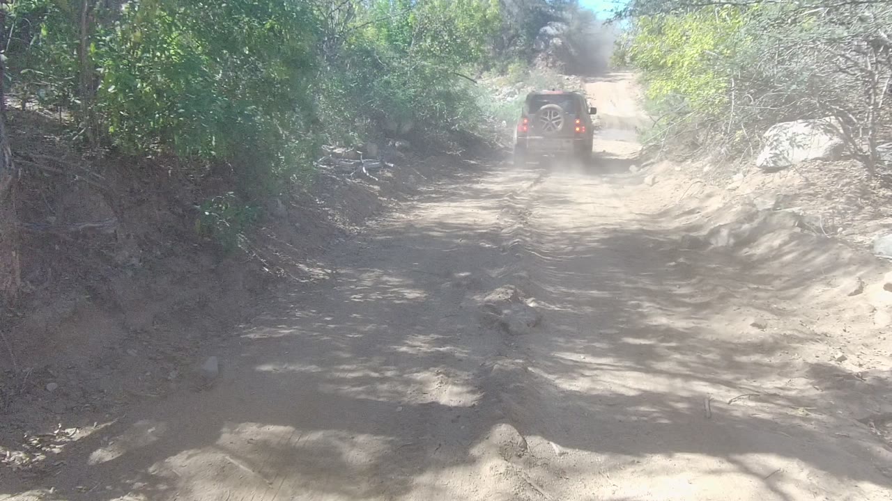 SUV farther up a narrow dirt trail with dust behind it