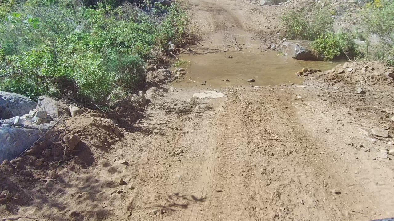 Vehicle approaches a shallow muddy puddle on the dirt road.