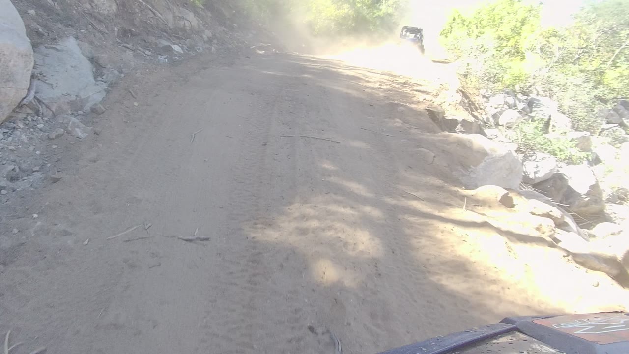 Forward view down a dirt road with dust and rocks along the shoulder