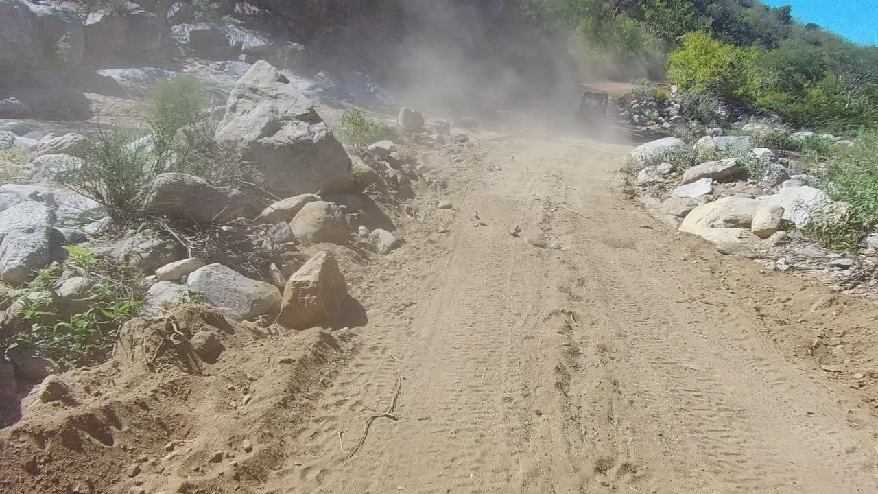 Rutted sandy road between rocks with dust ahead