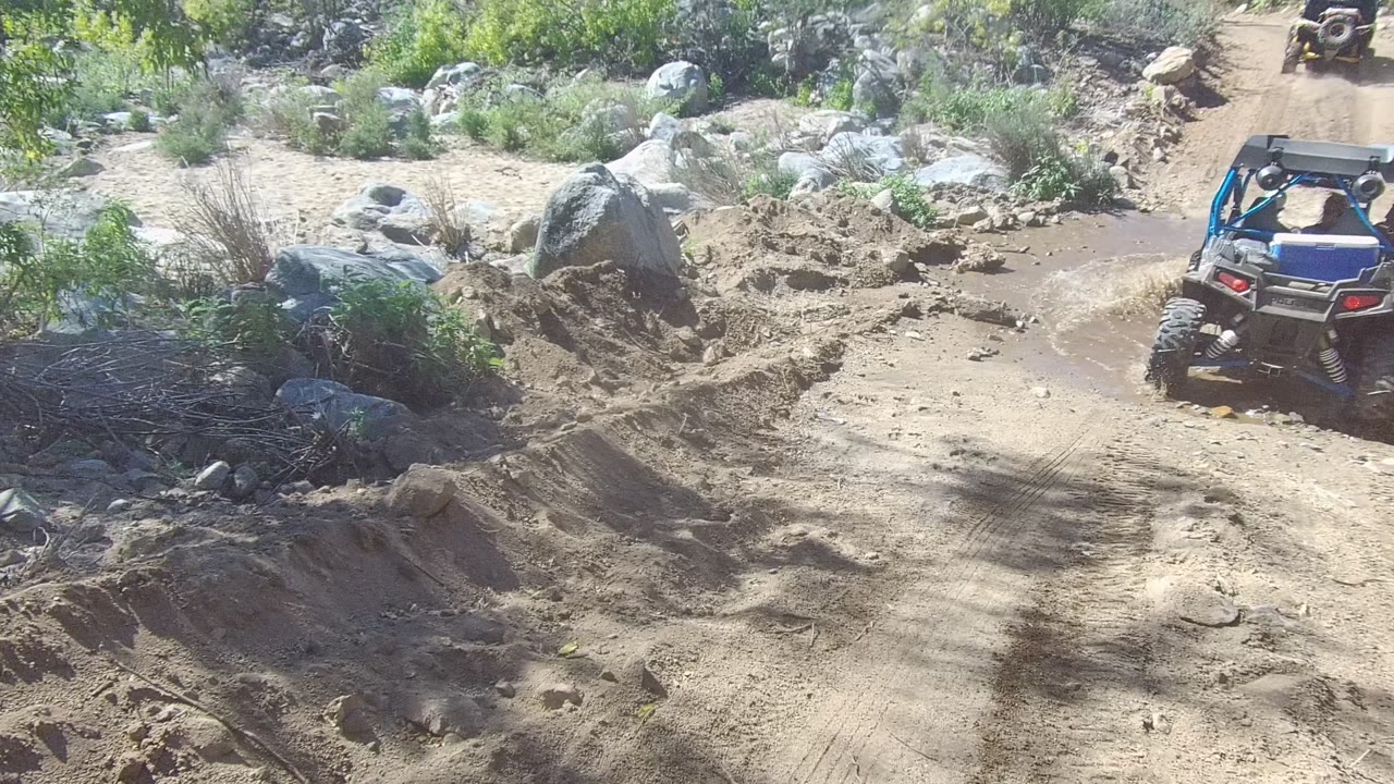 ATV moving toward a muddy puddle beside large rocks.