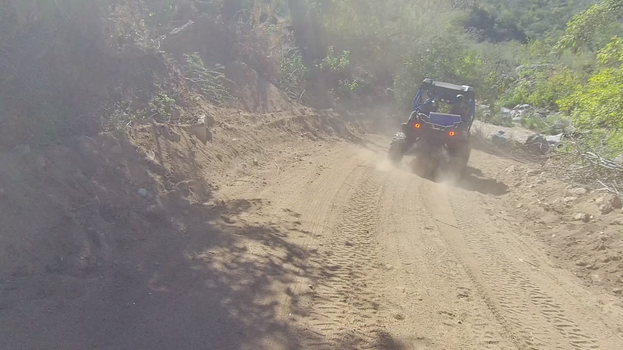 Blue off-road buggy drives away on a rutted sandy trail in Los Cabos, Baja California Sur, with dust behind it and no visible people.