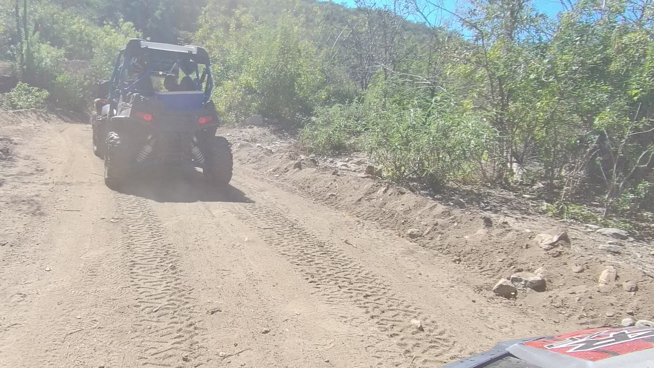 Off-road vehicle farther along a pale dirt road bordered by brush.