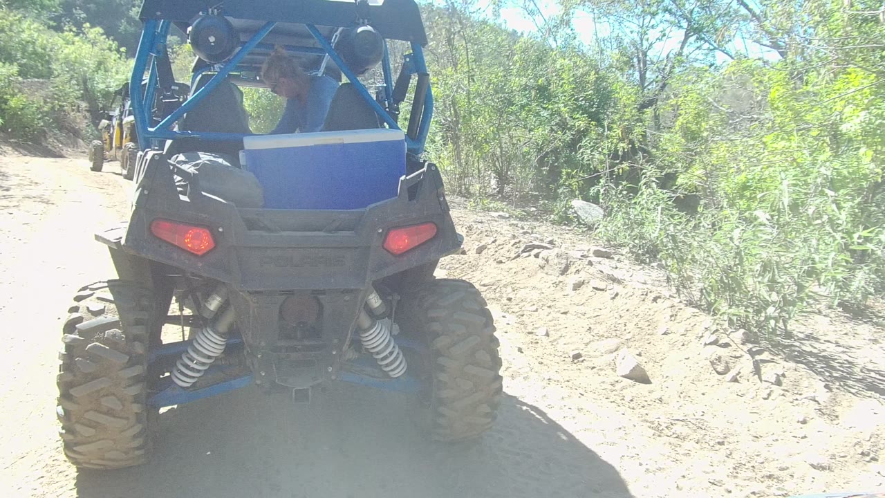 Blue UTV continues along the dirt trail under bright sun.