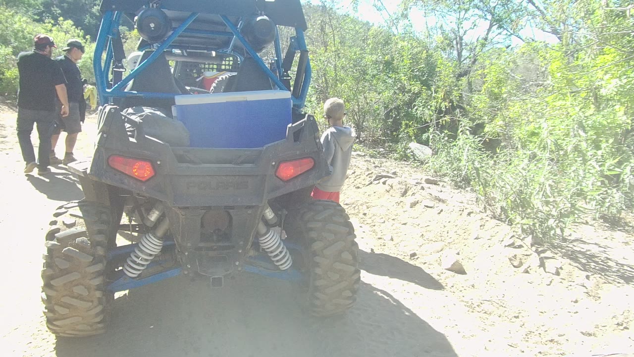 Blue off-road vehicle centered on a dusty path with two adults walking behind it.