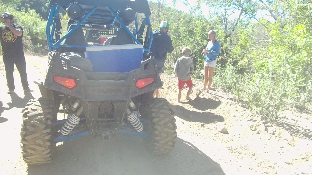 Group remains beside a blue off-road vehicle in bright brush terrain