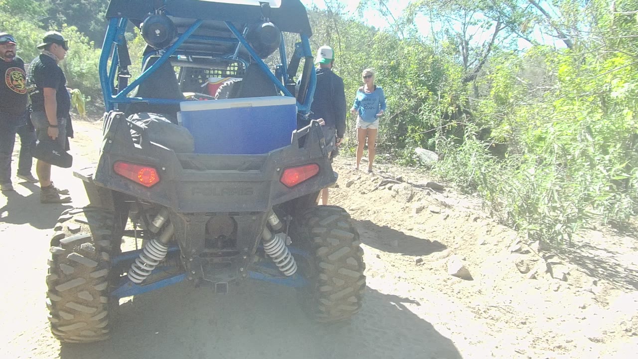 Off-road vehicle from behind with adults and a woman in a blue shirt nearby.