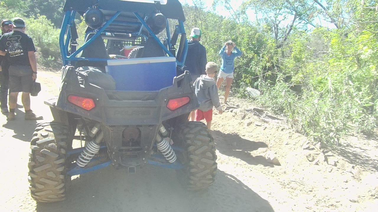 A child in red shorts is visible beside the rear of the off-road vehicle as adults stand on the dirt path in Los Cabos, Baja California Sur.