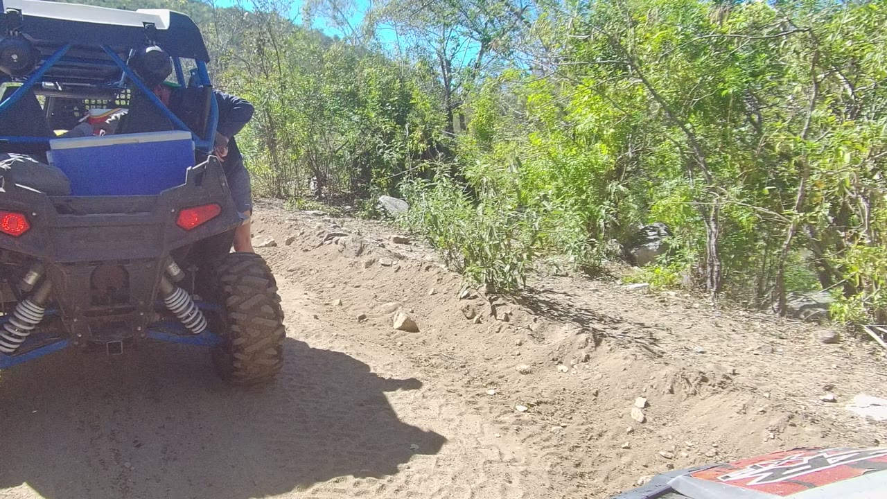 Off-road vehicle centered on a dusty trail with brush behind it.