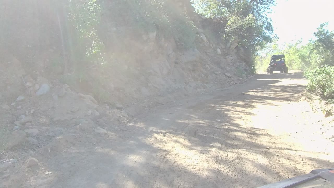 Off-road vehicle driving toward a sunlit bend on a dirt trail
