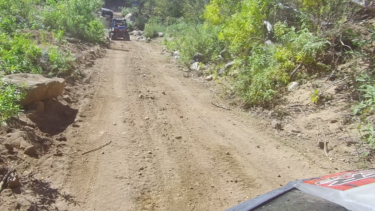 Dirt trail passing a large roadside boulder and brush