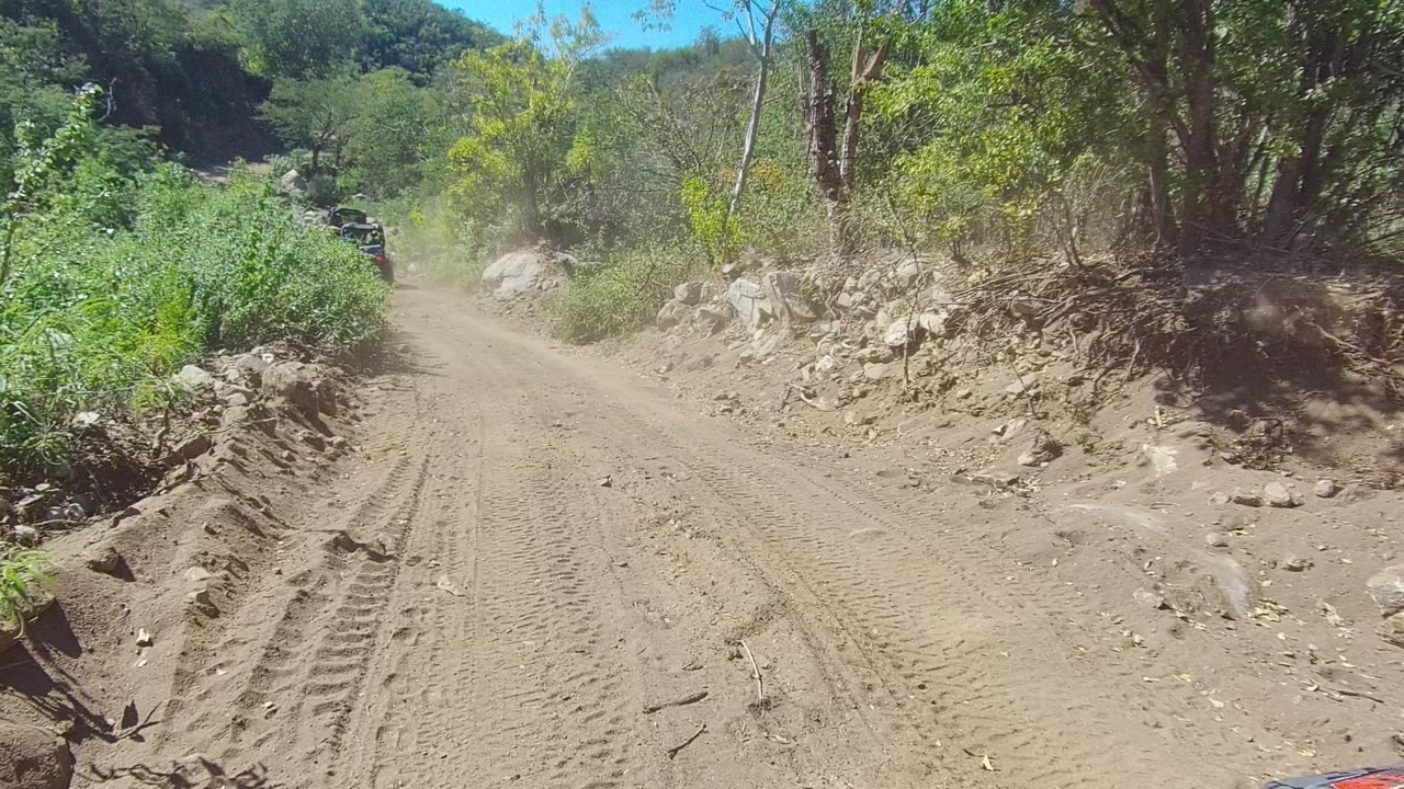 Unpaved road curving through brush with dust ahead.