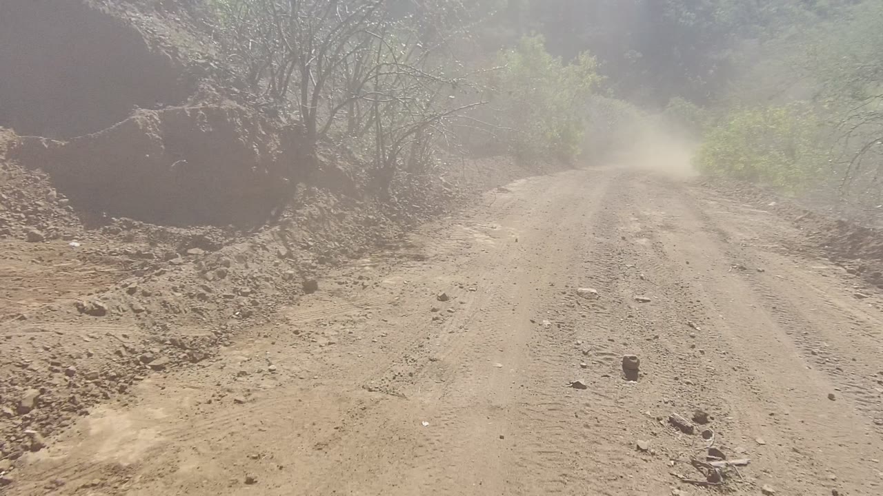Unpaved road beside an eroded dirt slope with bushes in haze.