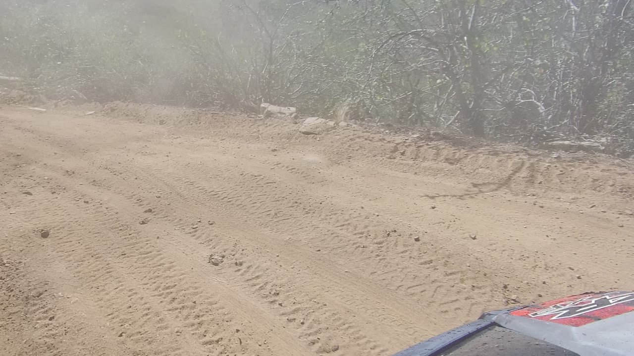 Sandy mountain road ahead with dust hanging over the track.