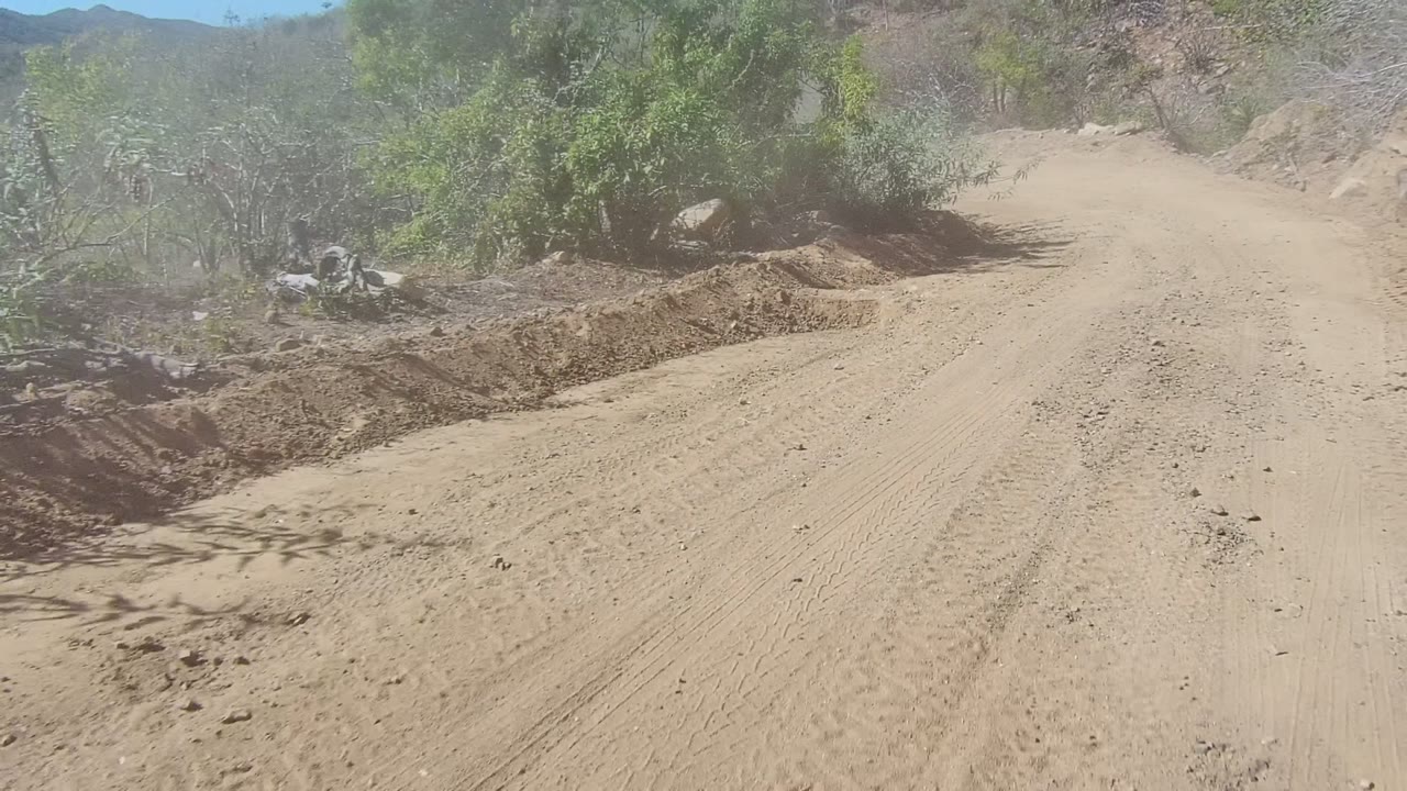 Dirt road ahead with brush, rocks, and dust haze.