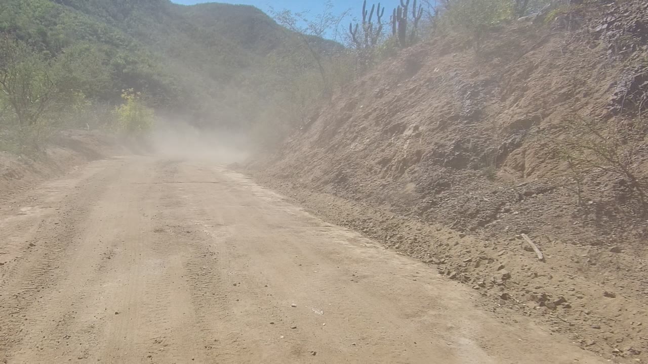 Straight dirt road with dust hanging over the track in bright sun.