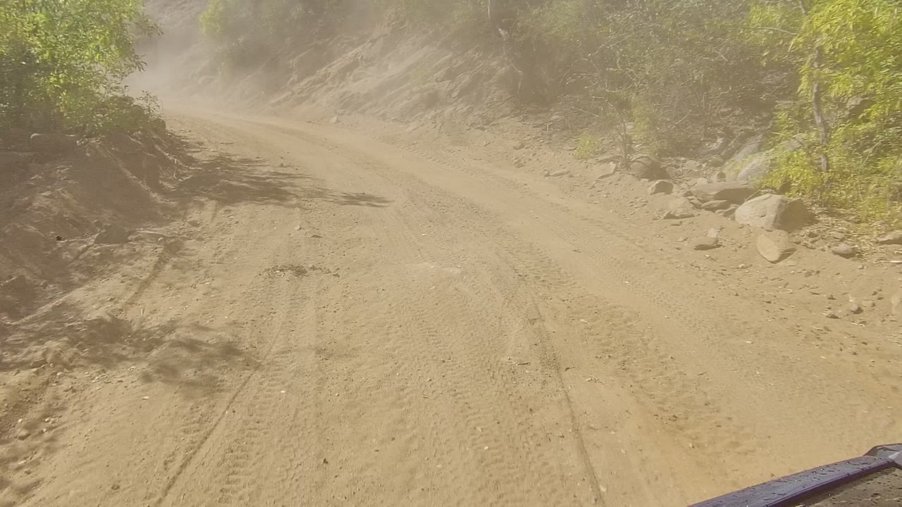 Rutted dirt road curving between rocky banks and sparse trees.