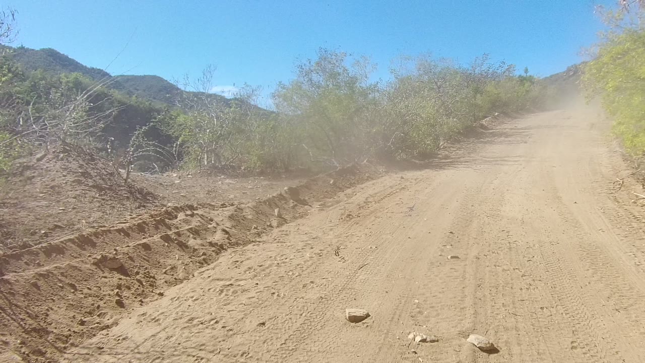 Sandy road with tire tracks, brush, mountains, and dust haze