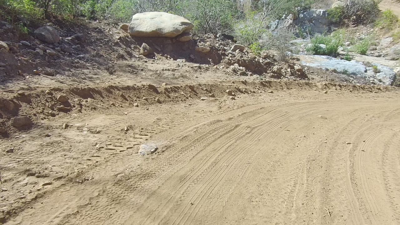 Dirt road curve beside rocks and scrub vegetation.