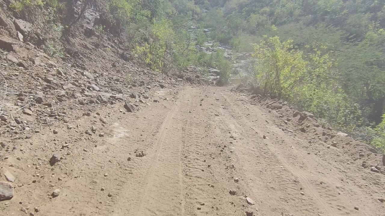 Unpaved road curving past loose rocks toward greenery