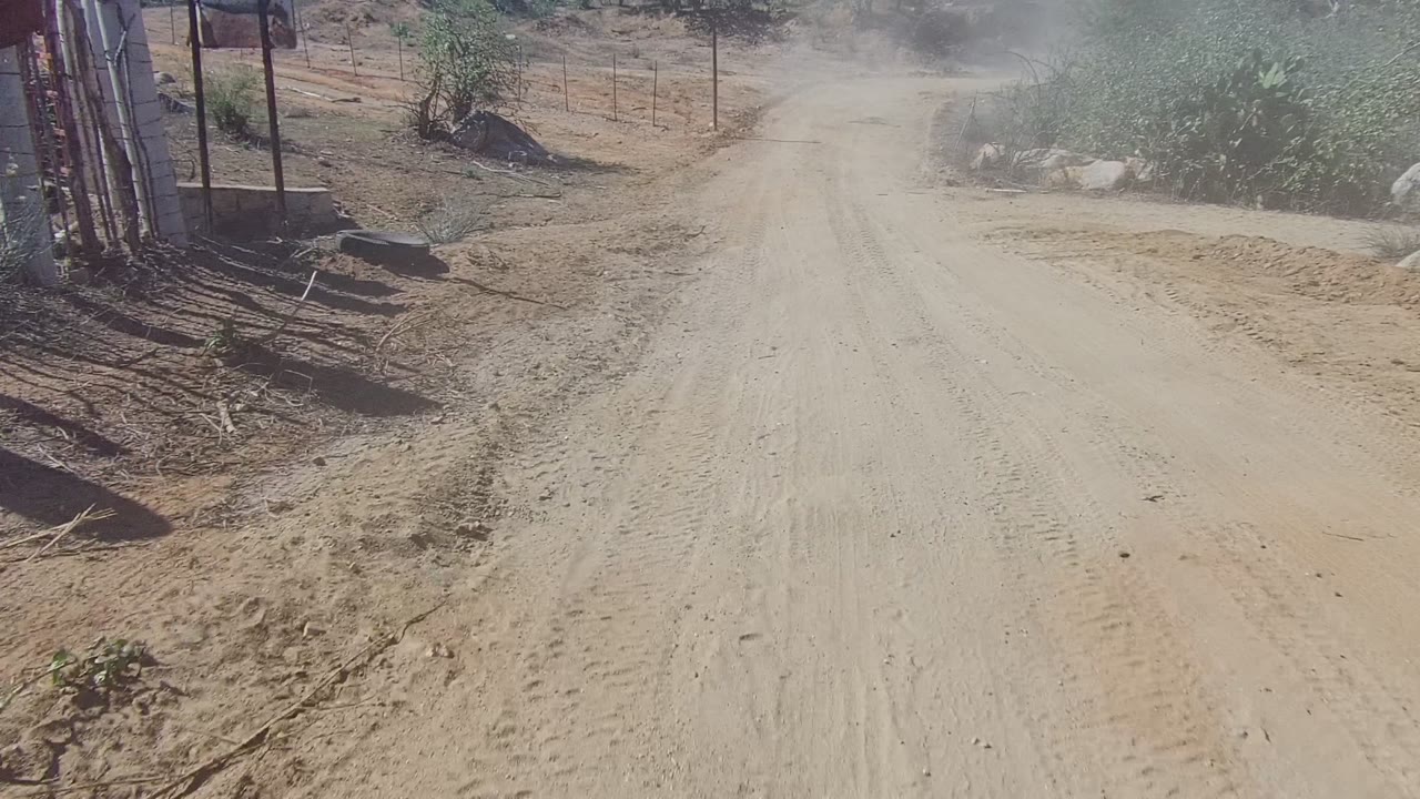 Sandy road curving through dry scrub with dust in the air.