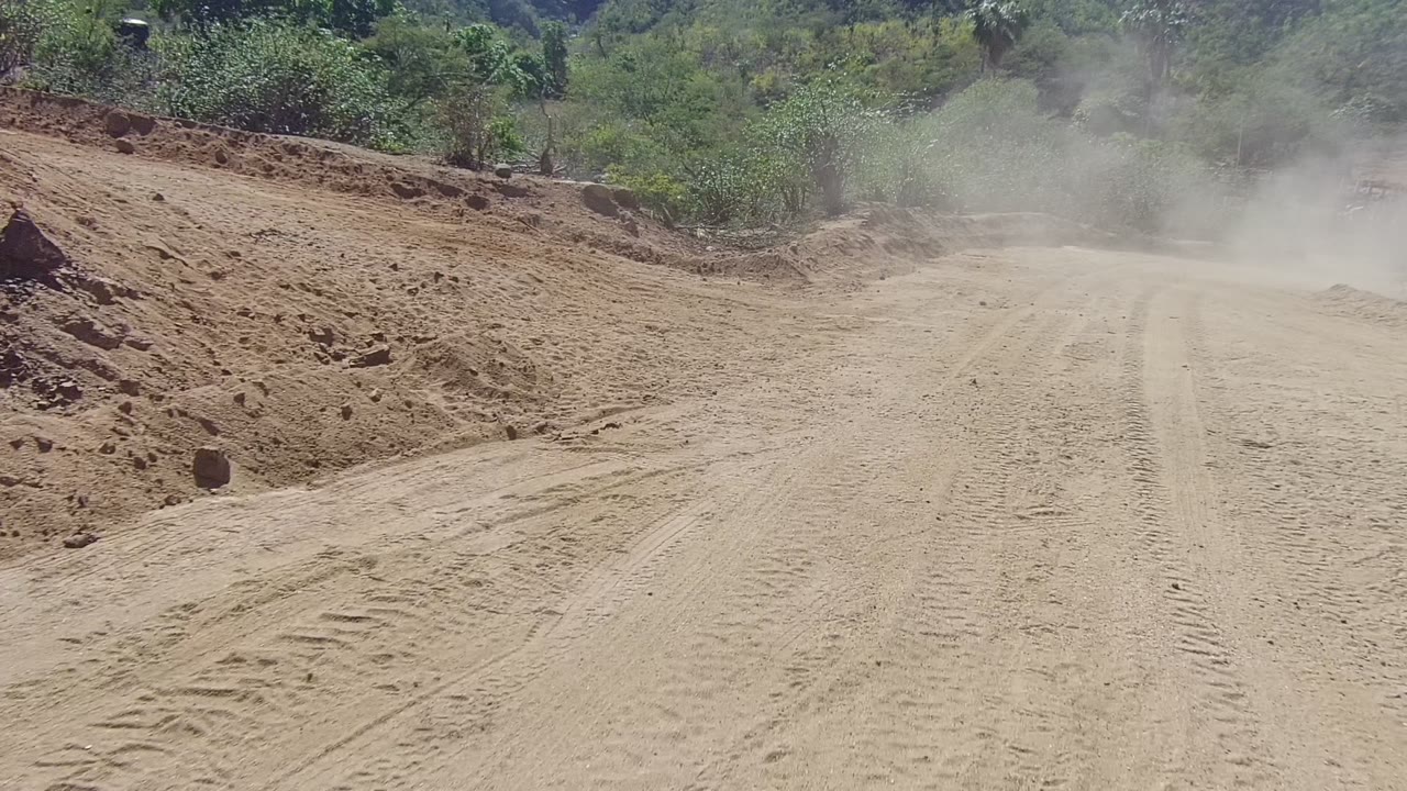 Dust cloud hanging over a sandy road bend.