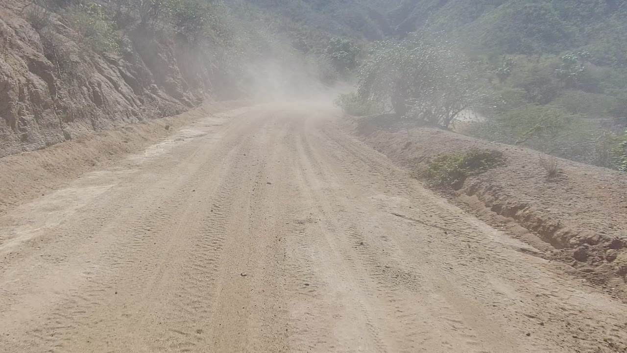 Unpaved road curving past eroded rock and brush under dust haze.