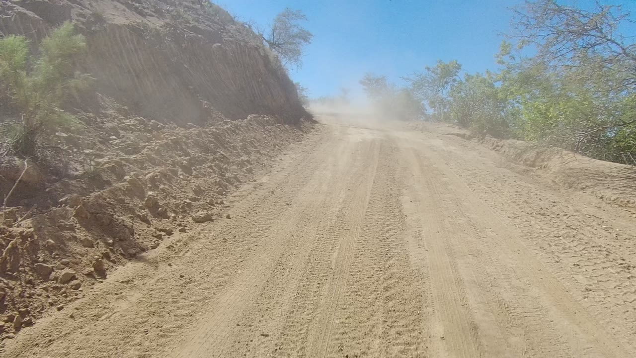 Unpaved road with tire tracks beside eroded earth bank.