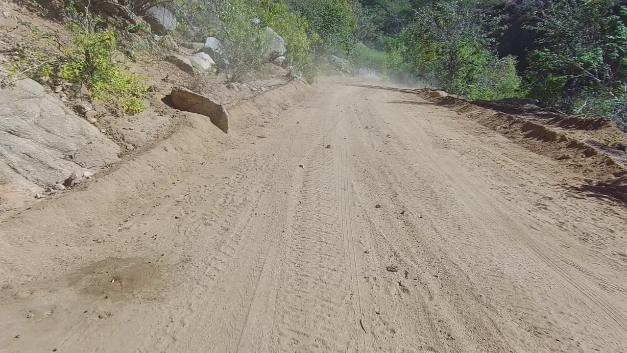 Unpaved road beside rocks with dust ahead