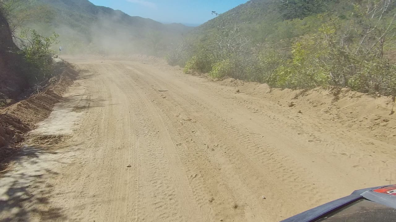 Dusty road ahead with brush and mountains in sunlight