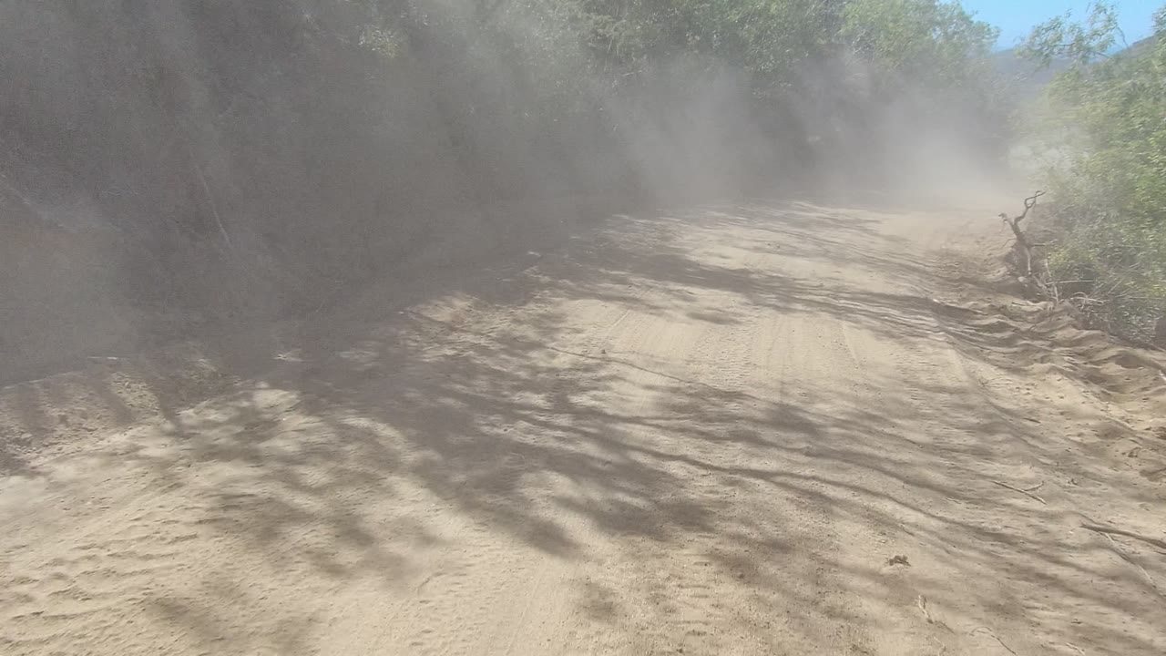 Sandy road with dust cloud and shadows across the track