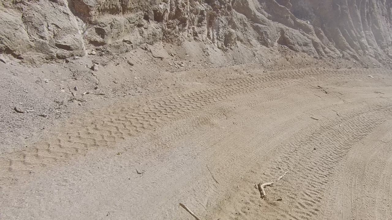 A sandy dirt road in Los Cabos, Baja California Sur runs beside an eroded rocky cut bank, with tire tracks across the foreground and no visible people.