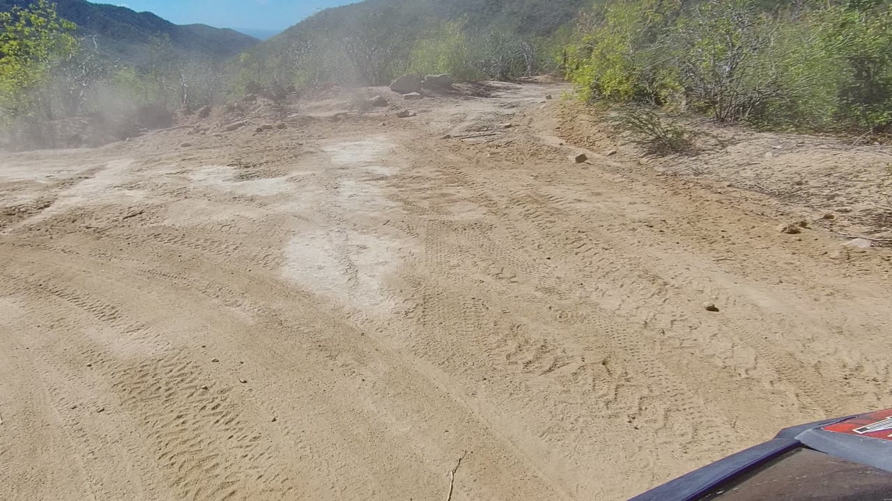 Sandy road curves through brush with dust hanging over the trail.