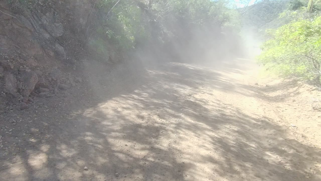 Unpaved road with dust haze against rocky roadside cut