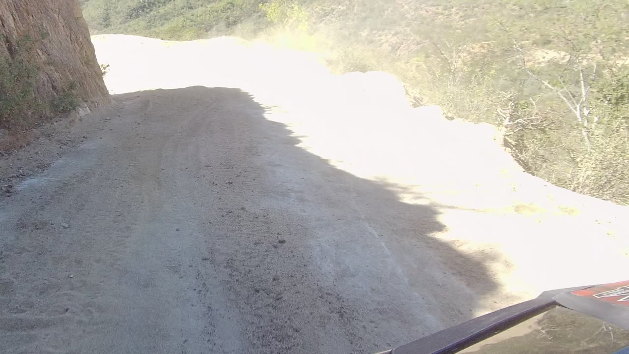 Dusty sandy road curving past a rocky hillside.