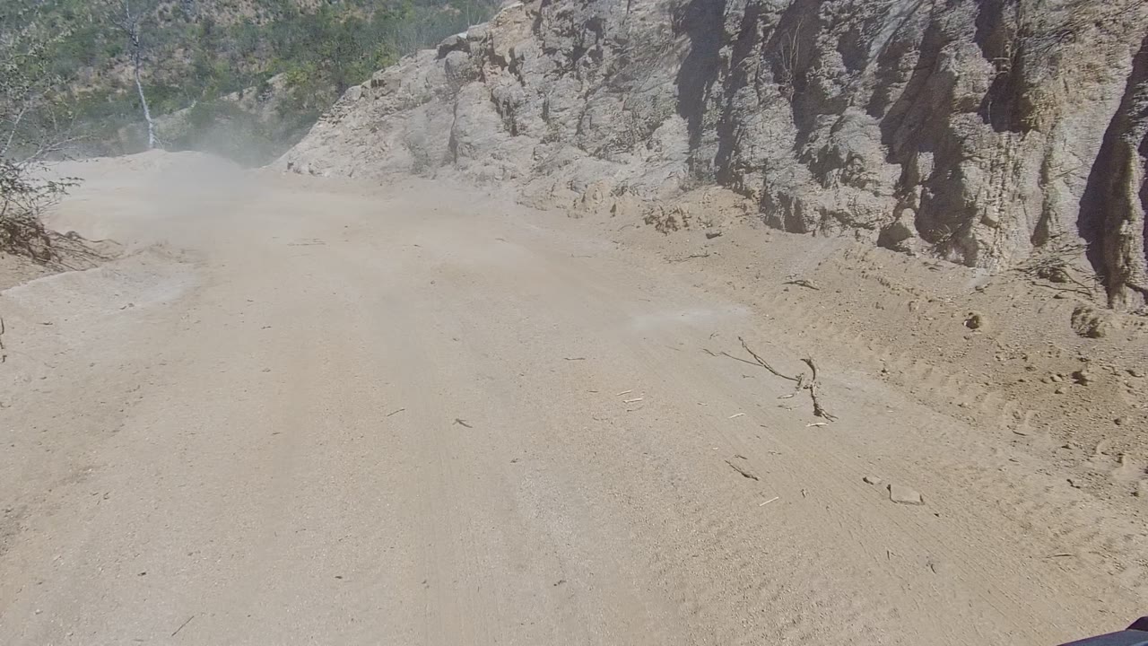 Sandy road curving past a steep eroded rock face.