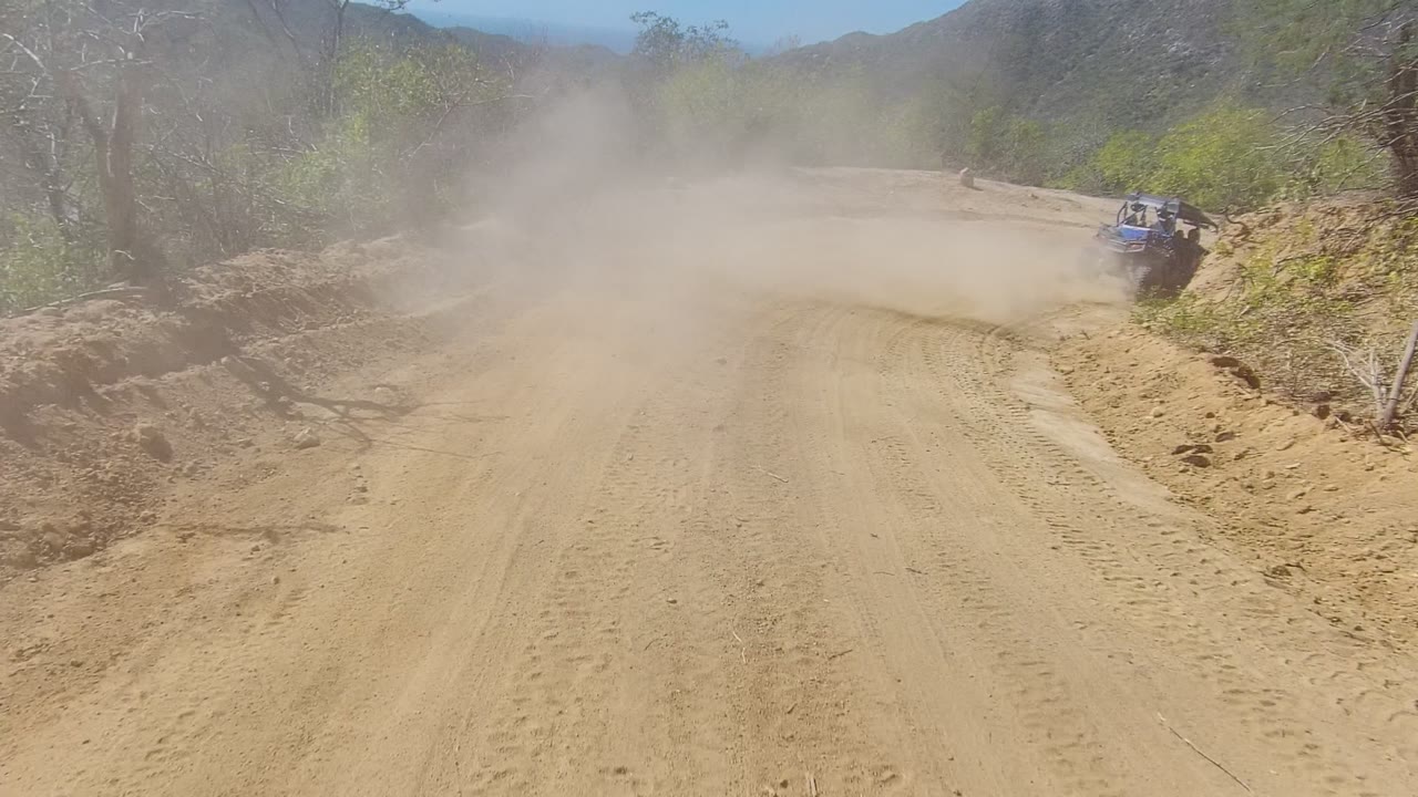 Dust cloud spreading across a sandy road with an off-road vehicle near the right side