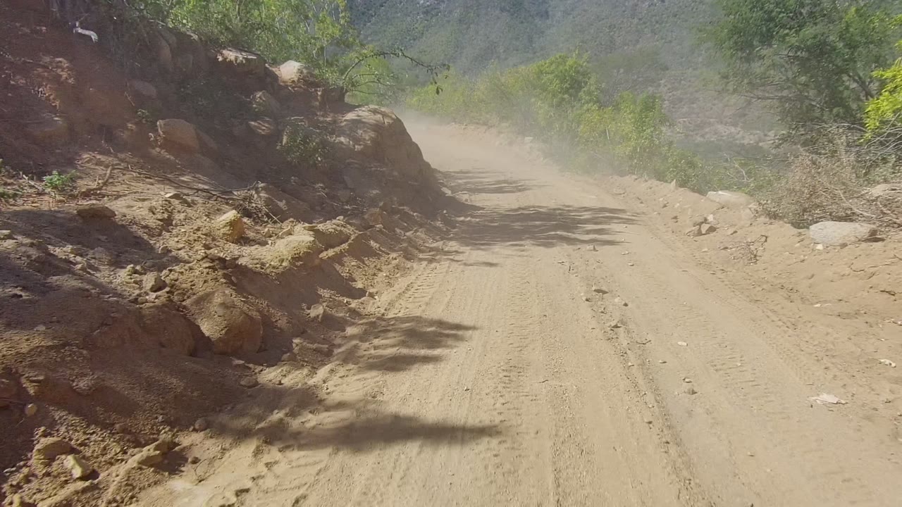 Sandy road beside a rocky cut with dust in the background.